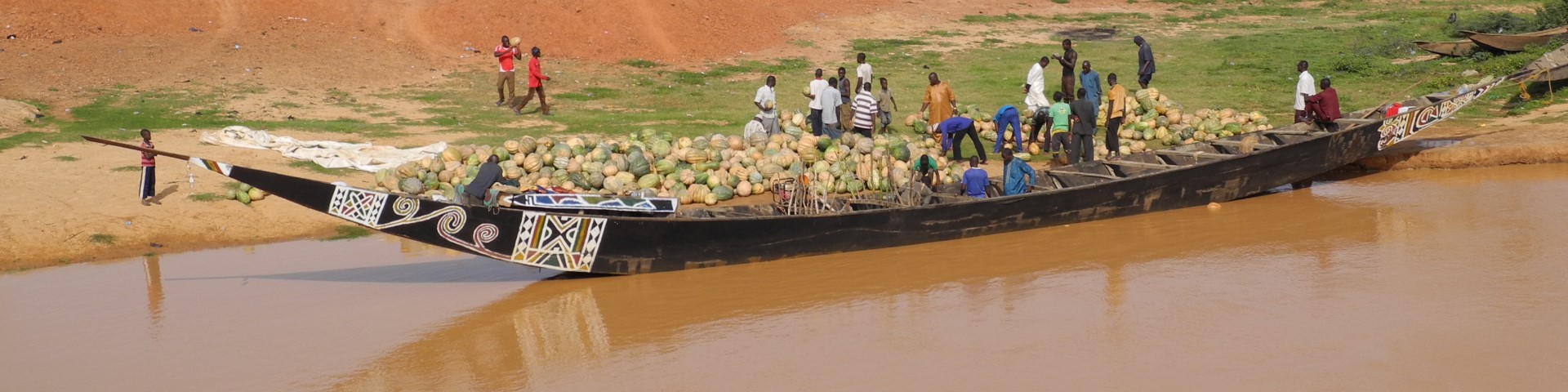 A large wooden boat loaded with pumpkins stops at a riverbank.