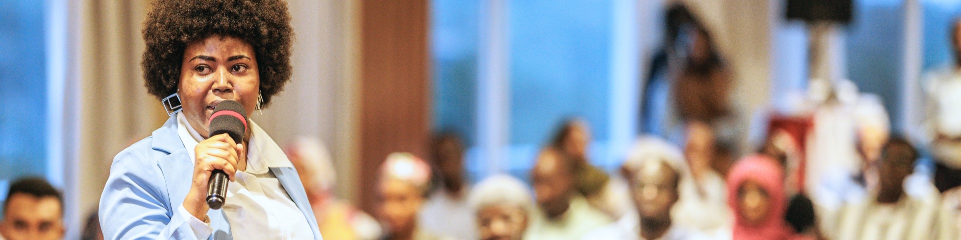 A woman speaks into a microphone before an audience.