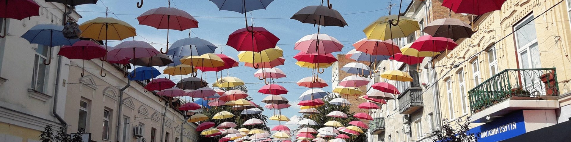 Lots of colourful umbrellas hanging from a net above a street.