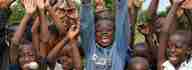 A group of children stretch their hands in the air, all laughing into the camera.