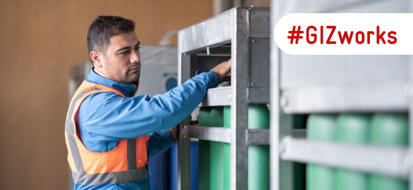 A man works with hydrogen cylinders that are stored in a steel container.