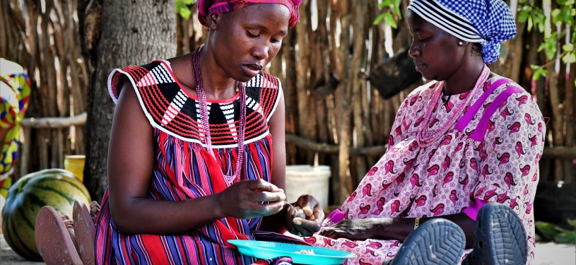 Two women sit together while one of them holds a marula nut in her hand.