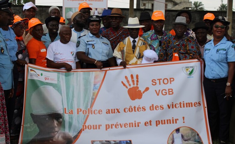 A group of individuals, including police officers and community members, hold a banner advocating the prevention and punishment of gender-based violence.