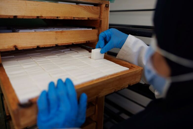 A person sorting soap stored on a wooden shelf.