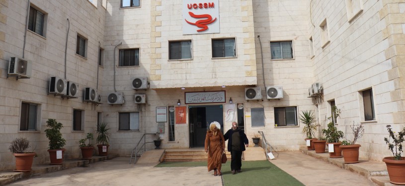 Two people walk in front of a hospital.