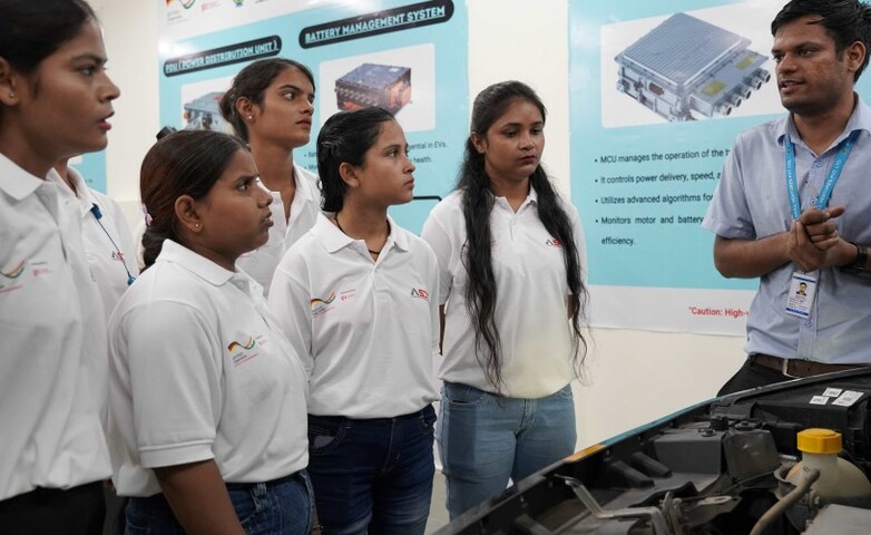 Participants listen closely to a trainer explaining components of an electric vehicle system in a training workshop.