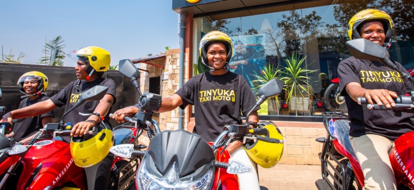 Women wearing helmets sit on motorcycles in front of a store