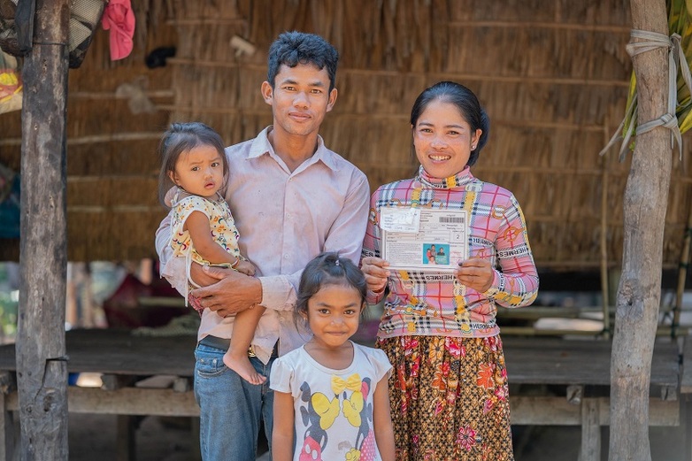 A family of four posing for the camera, holding a laminated equity card featuring their personal details, which gives them access to social assistance benefits and basic health care.