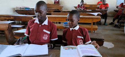 Two young boys sit at desks in a classroom and concentrate on their work.