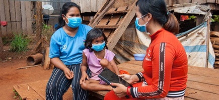 A woman holding a tablet is talking to a woman and her child.