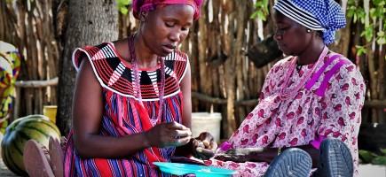 Two women sit together while one of them holds a marula nut in her hand.