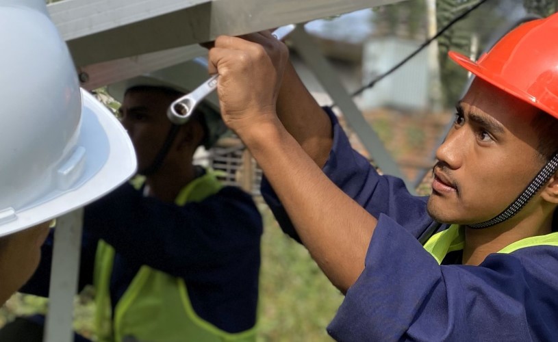 A man wearing a red safety helmet and holding a spanner examines a metal structure.