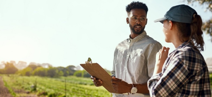 Two people are standing in front of a field and talking.