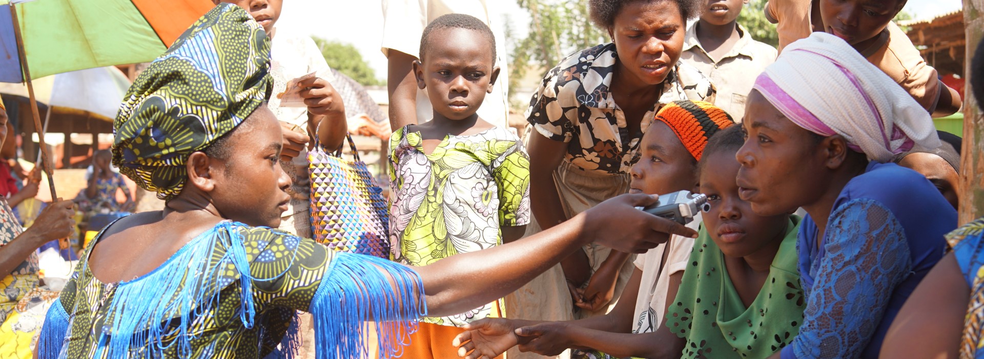 Reporter Dorcas Astery using a recording device to capture the thoughts and opinions of a group of women in Sanges.