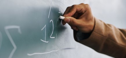 A person writing numbers on a blackboard with chalk.