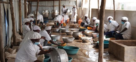 Employees wearing PPE are sitting at bowls in a food processing company.